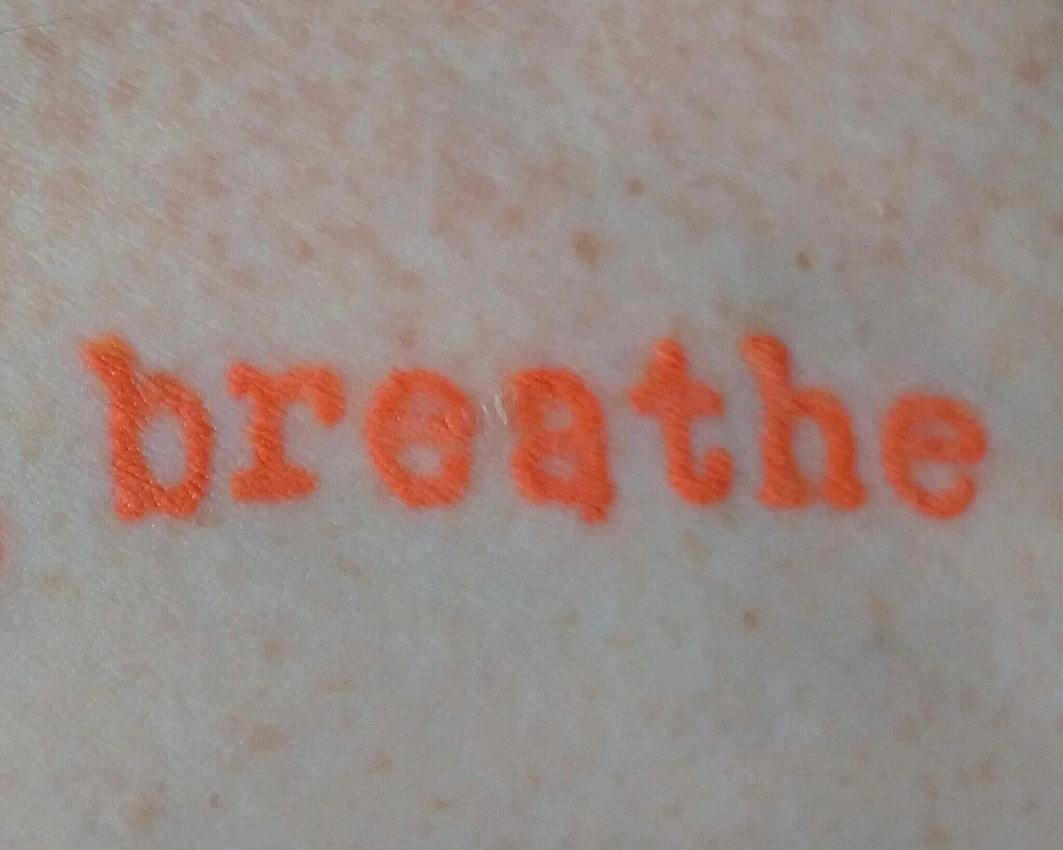 Orange tattoo of the word breathe.